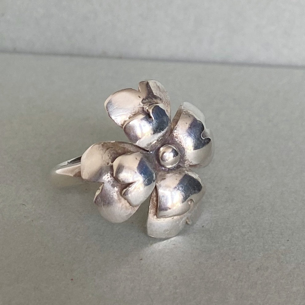 A sterling silver flower-shaped ring with textured petals and a polished center, displayed on a neutral gray surface.