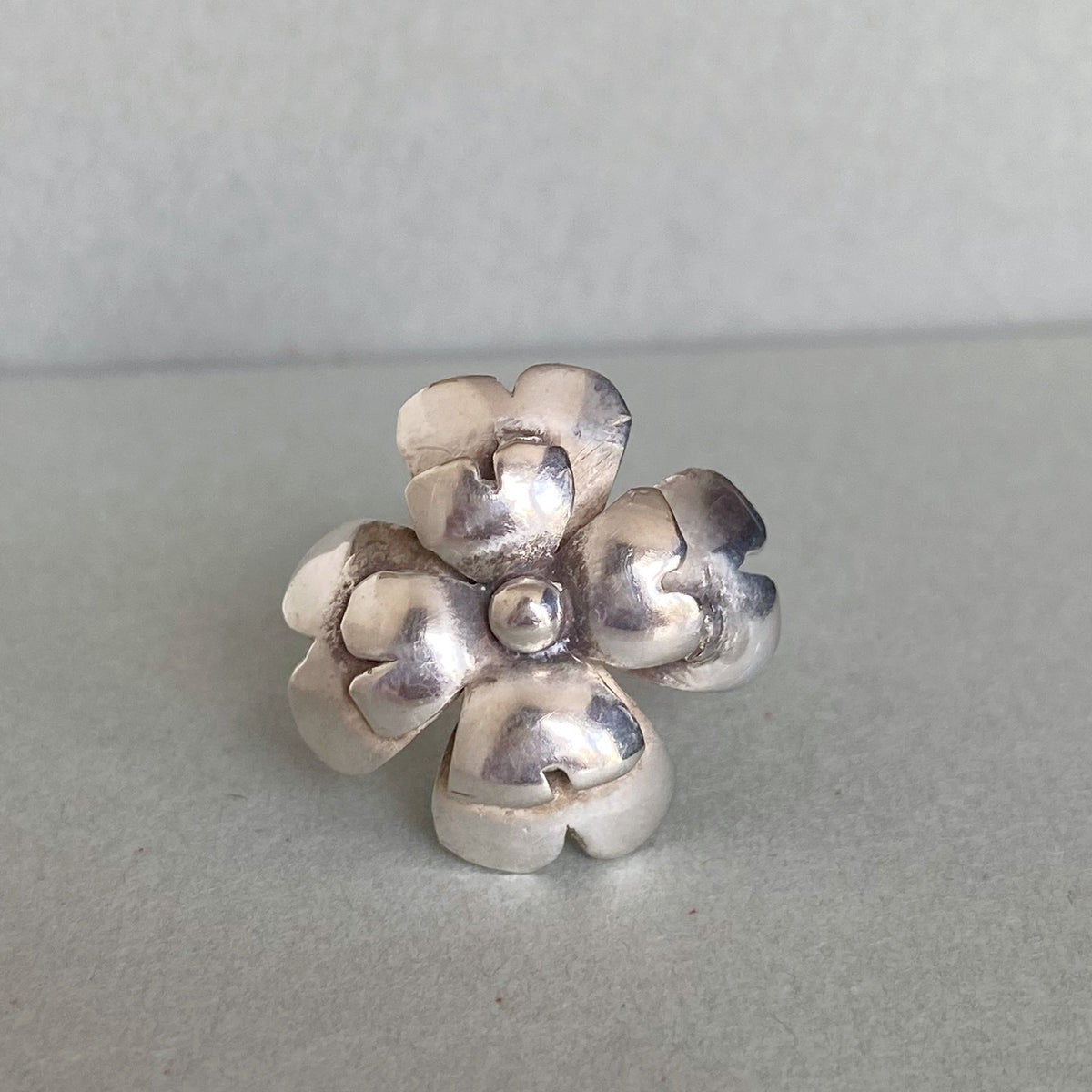 A sterling silver flower-shaped ring with a textured, hammered finish, displayed on a neutral gray surface.