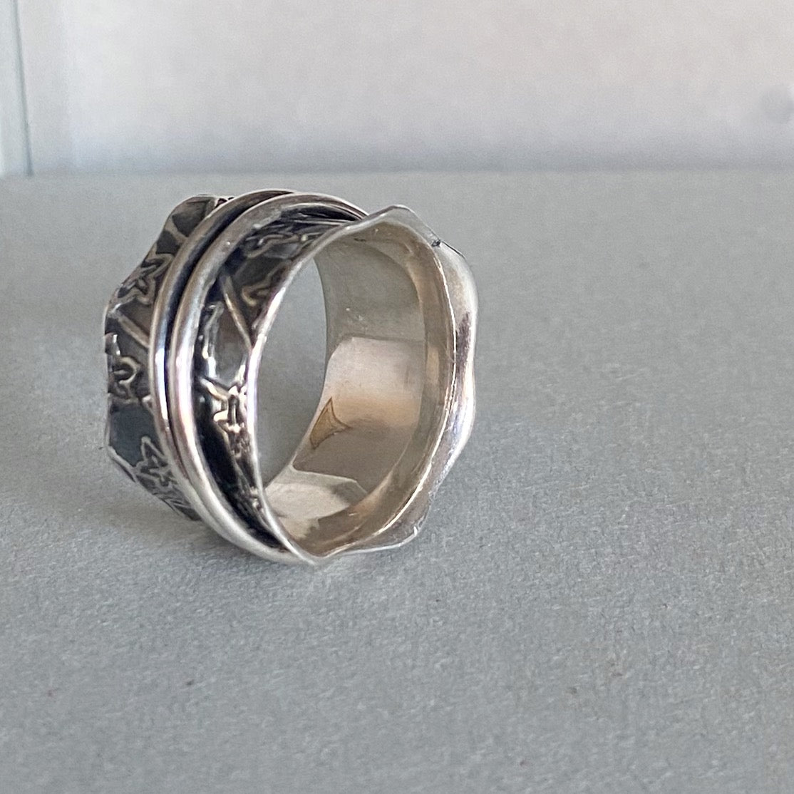 A sterling silver spinner ring with engraved details, resting on a textured gray surface.