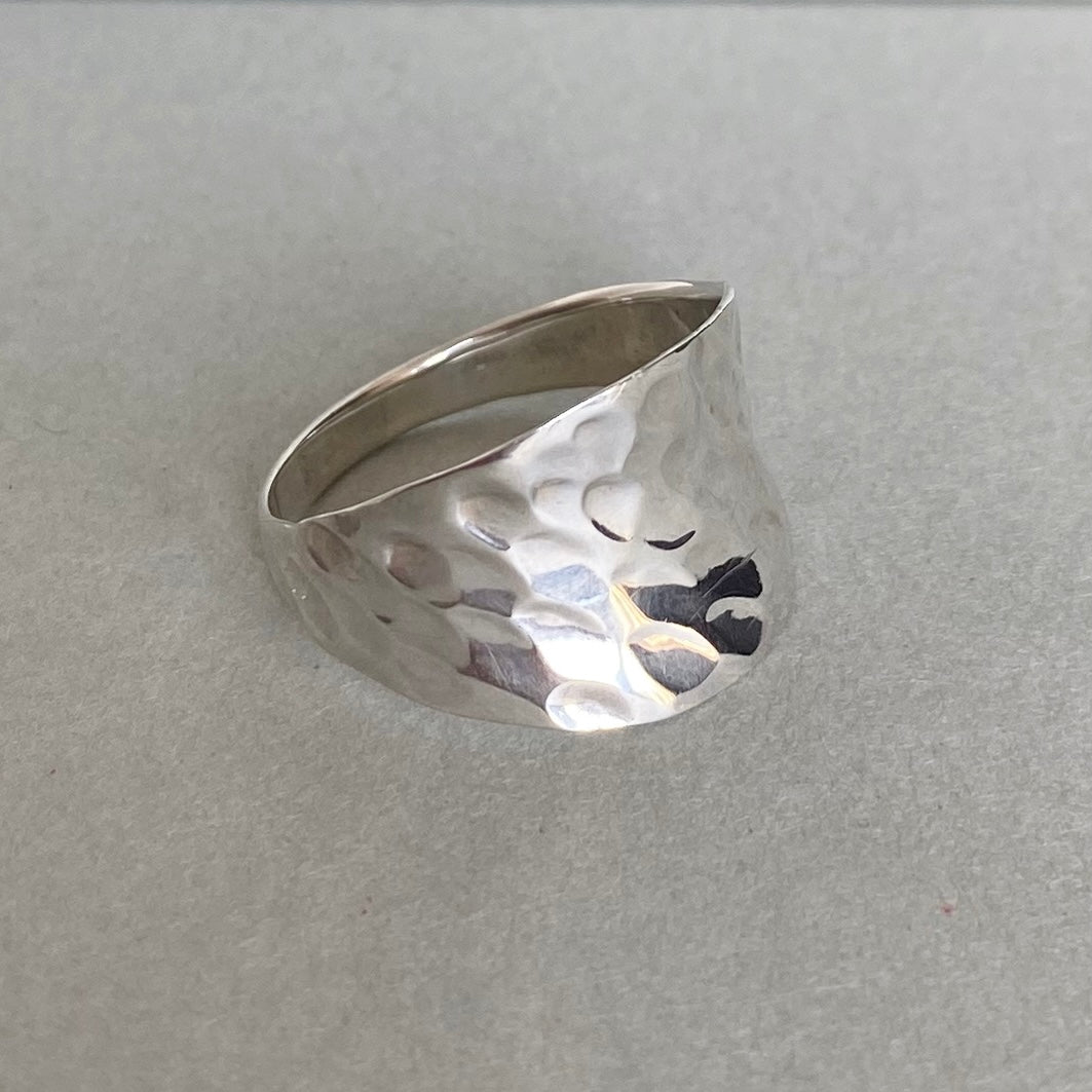 A hammered sterling silver ring with a wide, open-top band, resting on a textured gray surface.