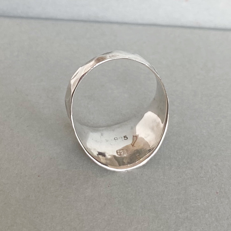 A hammered sterling silver ring with a wide, rounded band, photographed on a neutral gray textured surface.