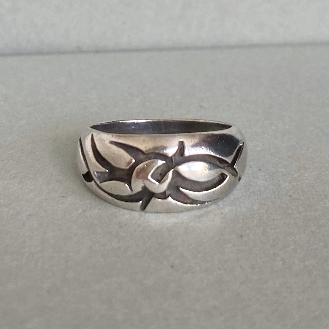 A sterling silver band ring with a raised abstract tribal-style design, photographed on a neutral gray textured surface.
