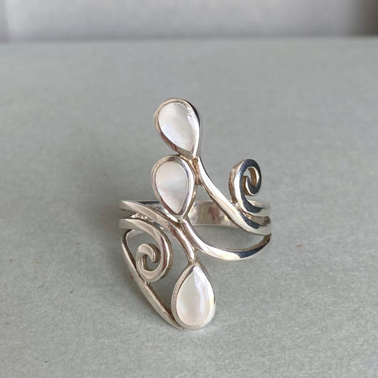 A silver ring with three teardrop-shaped white mother-of-pearl inlays, displayed on a neutral gray surface.