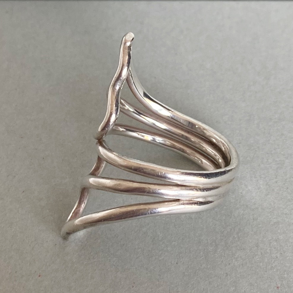 A polished silver wrap ring with a unique, organic wavy design, displayed on a neutral gray background.