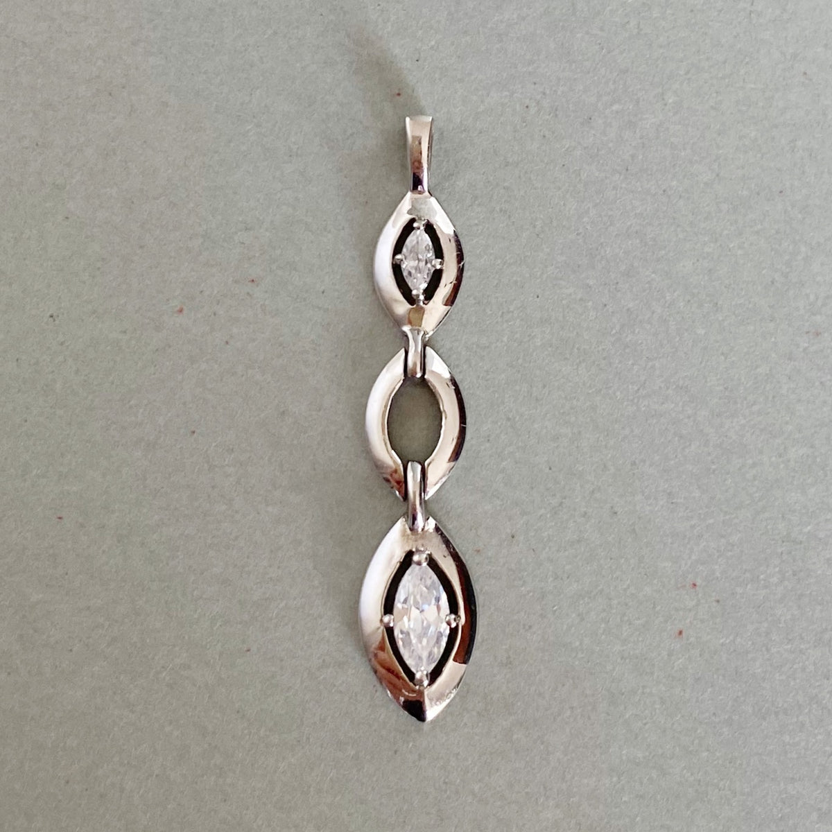 A silver-toned pendant featuring three vertically stacked marquise-cut gemstone settings, displayed on a neutral gray background.