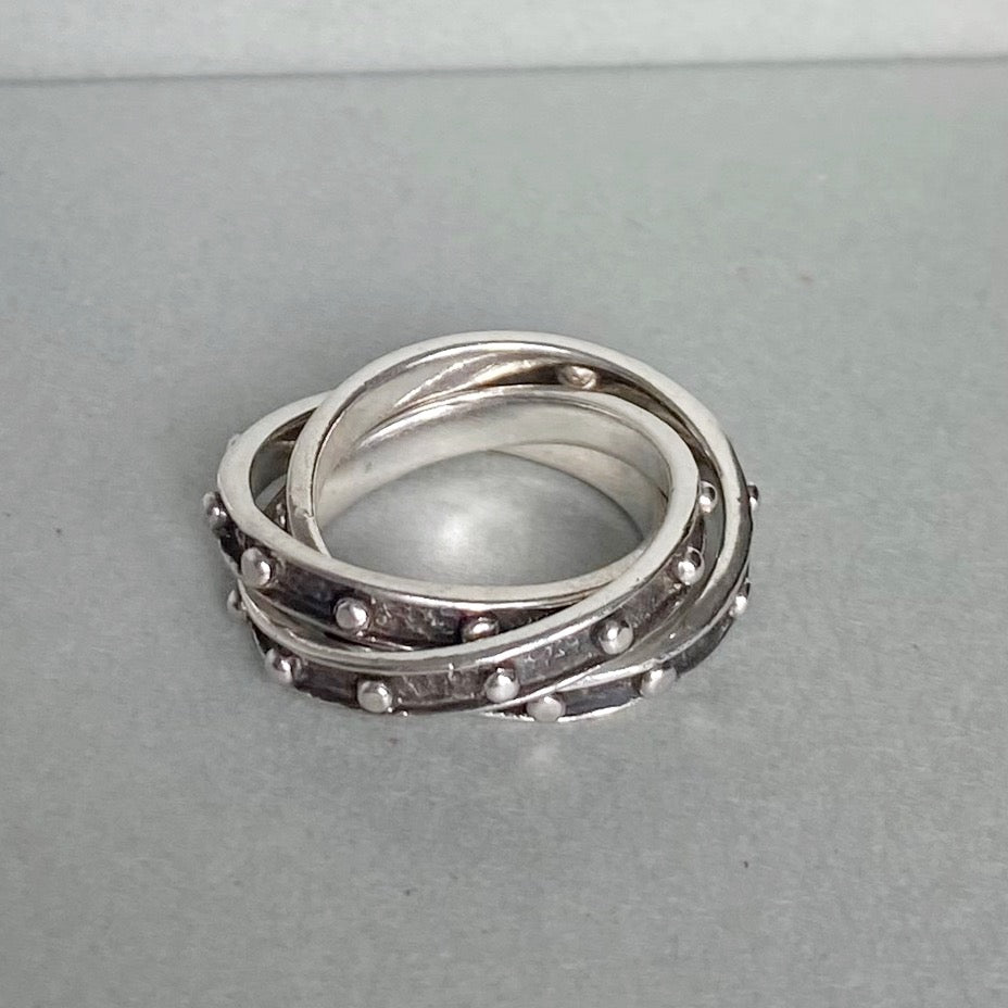 A stack of three silver rings with textured bands and small raised dots, displayed on a neutral gray surface.