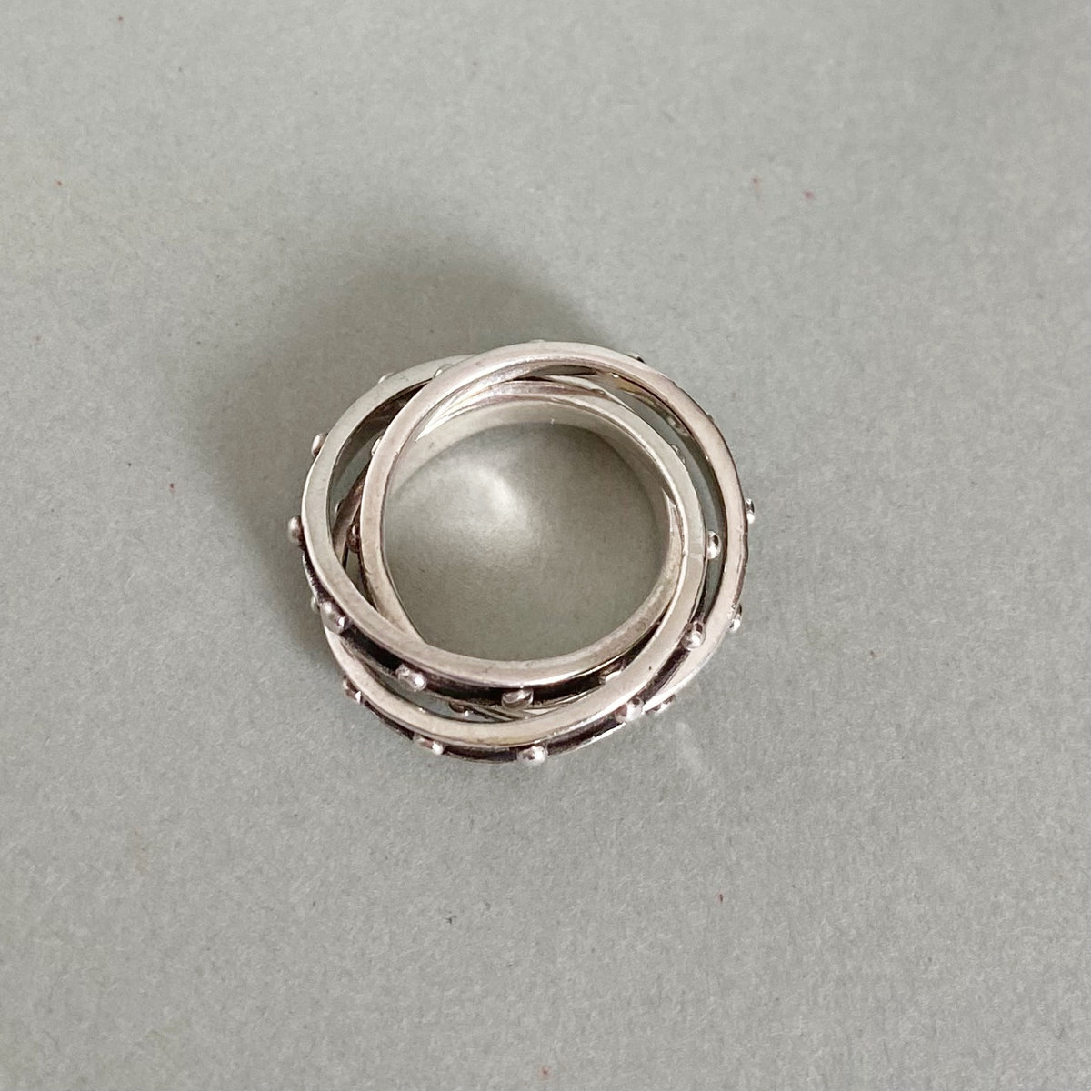 A silver-toned multi-band ring with a textured, beaded outer band, photographed on a neutral gray background.