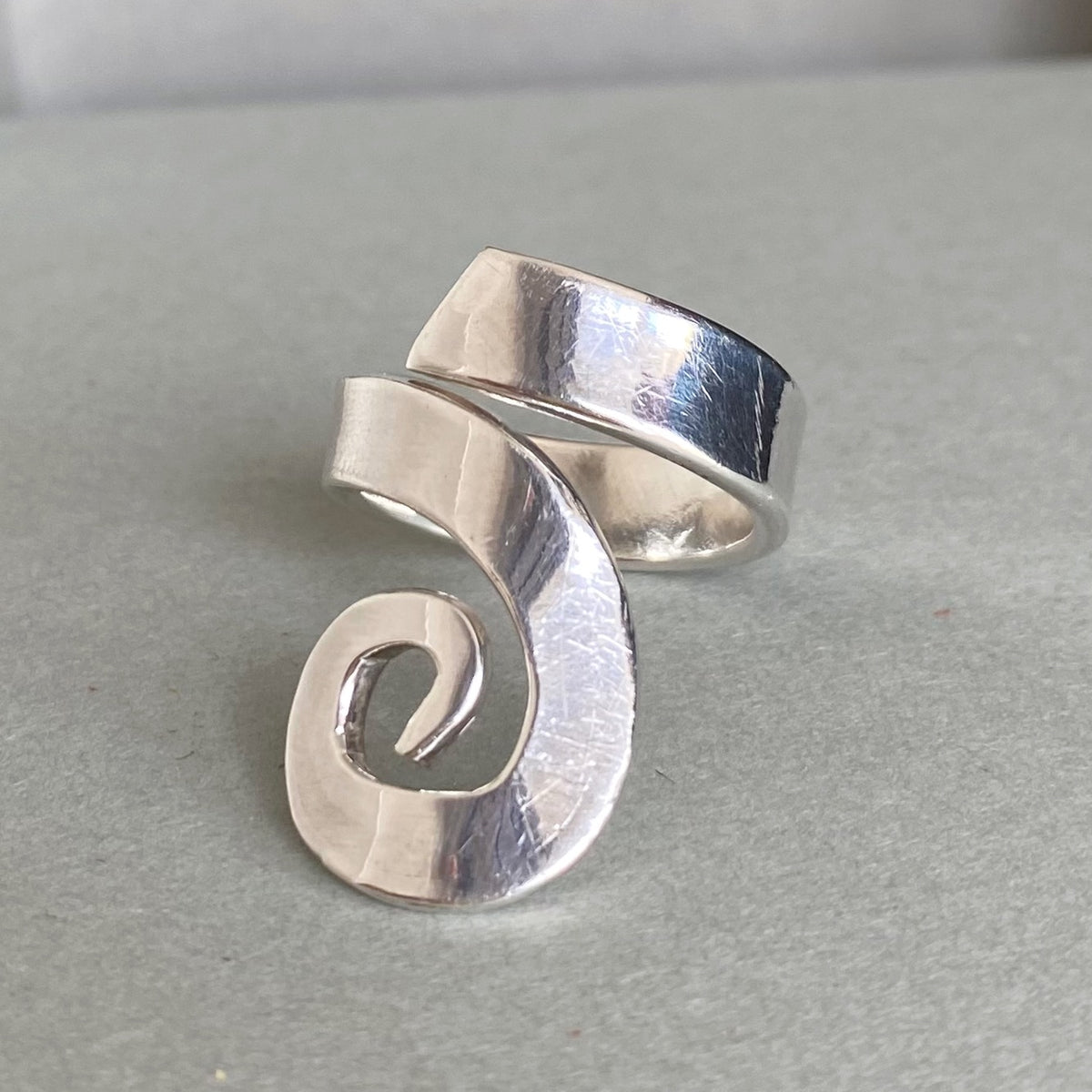 A silver spiral-shaped ring with a hammered texture, displayed on a neutral gray background.