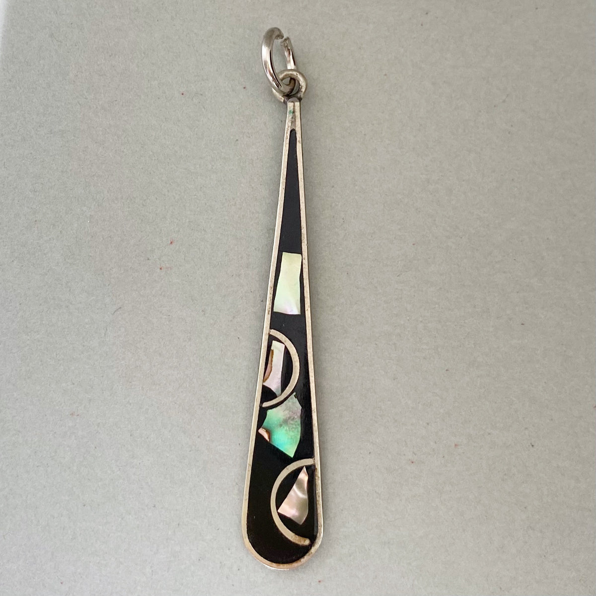 A sterling silver teardrop-shaped pendant with a black inlay and geometric abalone shell mosaic accents, shown on a neutral gray background.