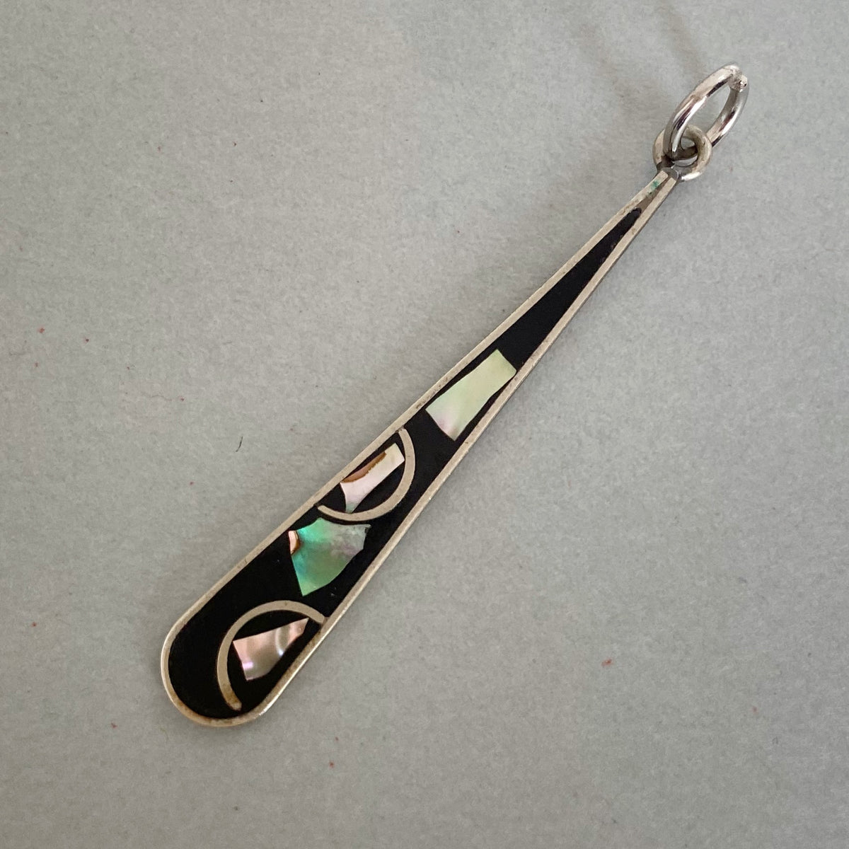 A sterling silver teardrop pendant featuring black inlay and geometric mother-of-pearl abalone shell accents in green, pink, and cream, displayed on a neutral gray background.
